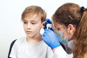 Audiologist using an otoscope to examine a young boy's ear