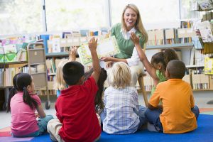Children in a classroom listening to a teacher read a story 