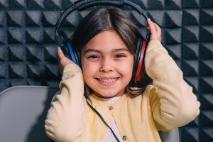 Smiling little girl wearing headphones in a soundproof room while having her hearing tested by a pediatric audiologist