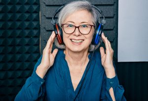 Smiling woman wearing headphones in a soundproof booth while working with an audiologist